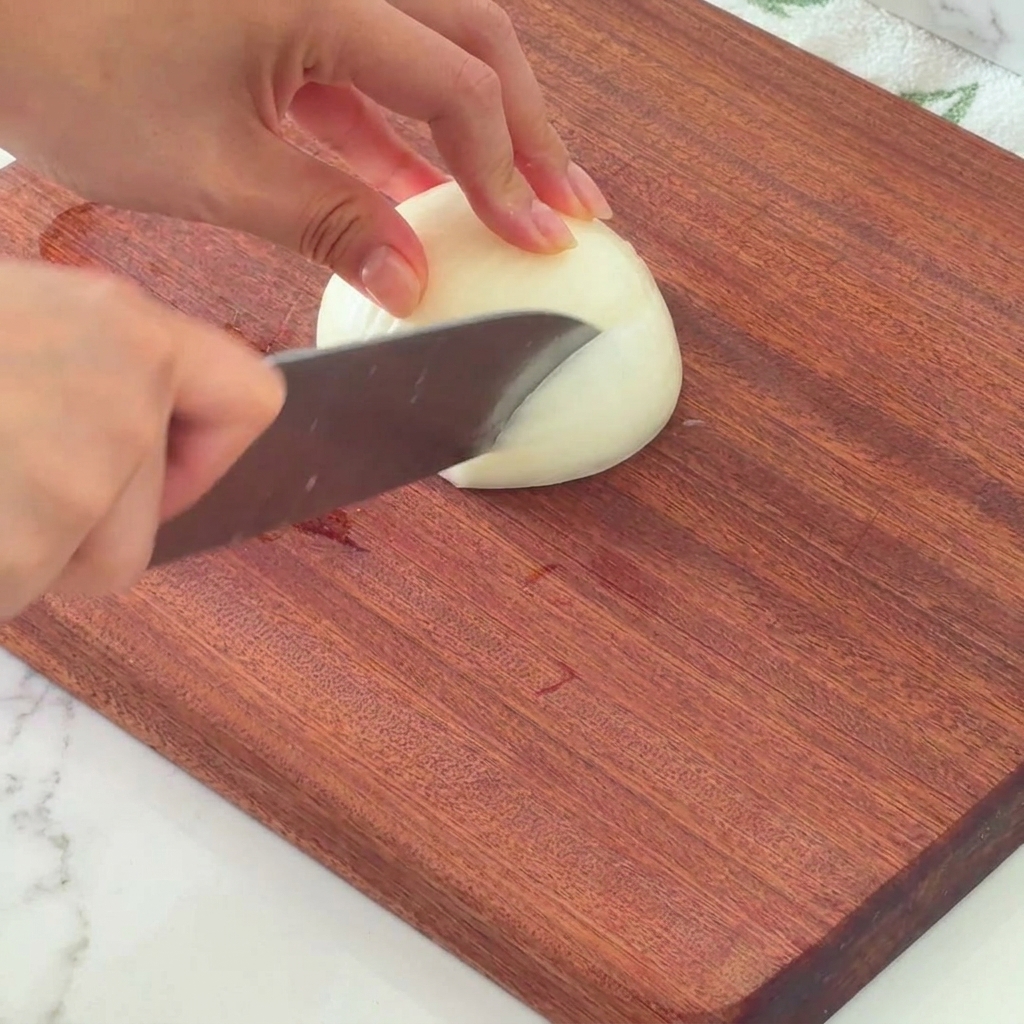 Eine halbe weiße Zwiebel wird sorgfältig auf einem Holzbrett gewürfelt.