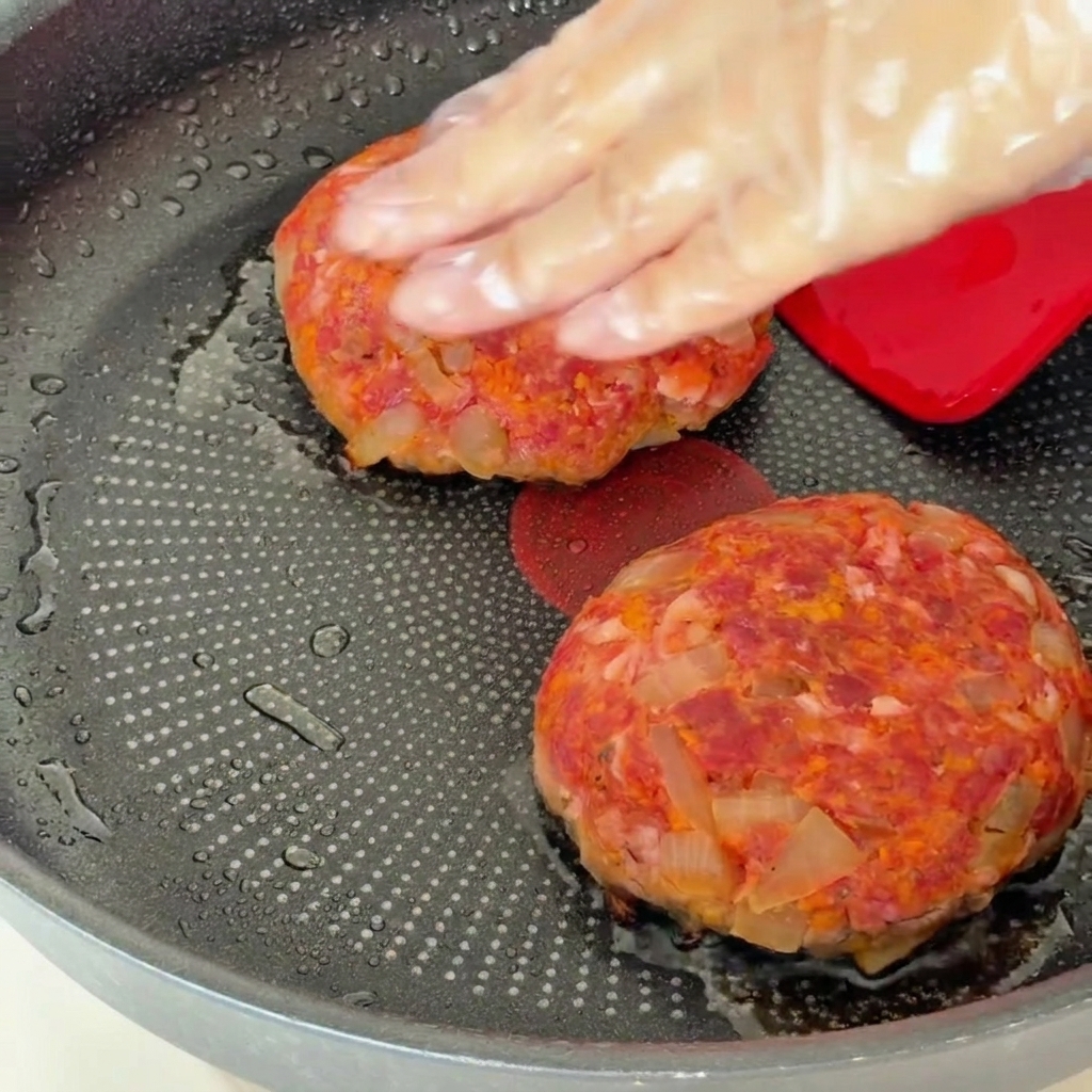 Hamburger-Patties in einer Pfanne, die nach dem Wenden mit einem Deckel abgedeckt werden.