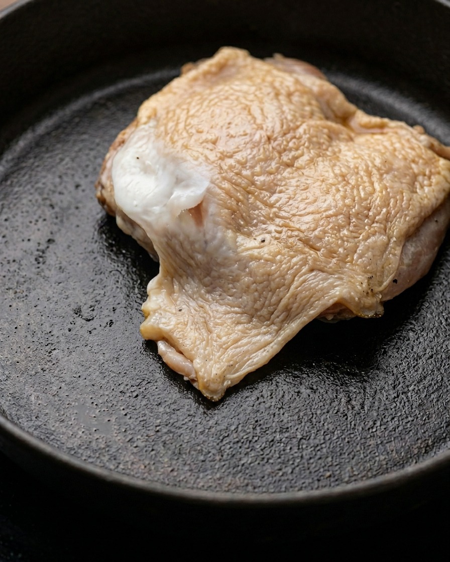 Ein Stück mariniertes Hähnchenkeulenfleisch bräunt in einer Pfanne mit geschmolzener Butter.