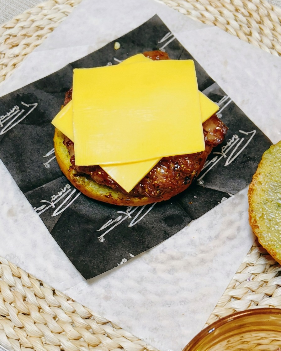 Nahaufnahme eines Burgers, bei dem eine Scheibe Schmelzkäse auf dem Hähnchen-Patty liegt, gekrönt von frischen Gurkenscheiben.