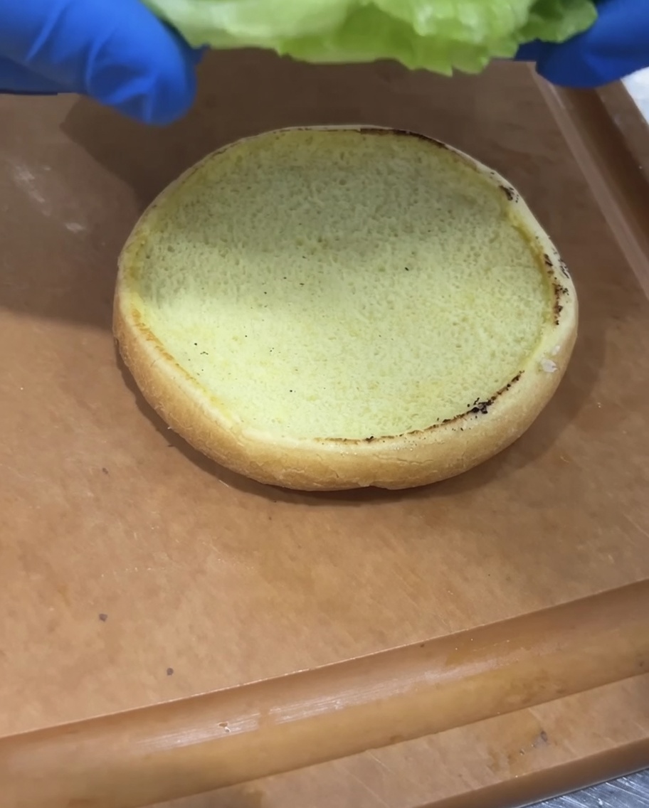 Frischer Salat und Tomatenscheiben, die auf ein getoastetes Burgerbrötchen gelegt werden.