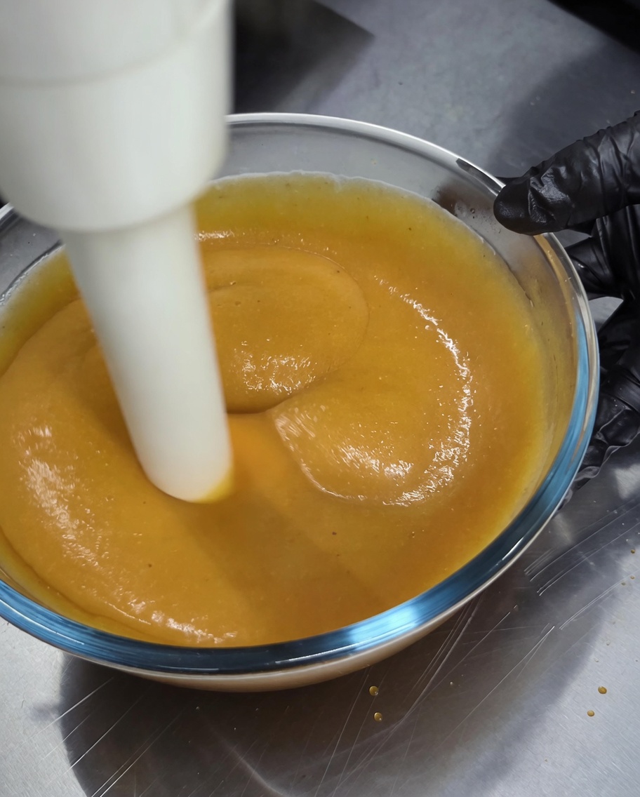 Ein Stabmixer wird verwendet, um eine dicke, goldbraune Sauce in einer Glasschüssel zu mixen.