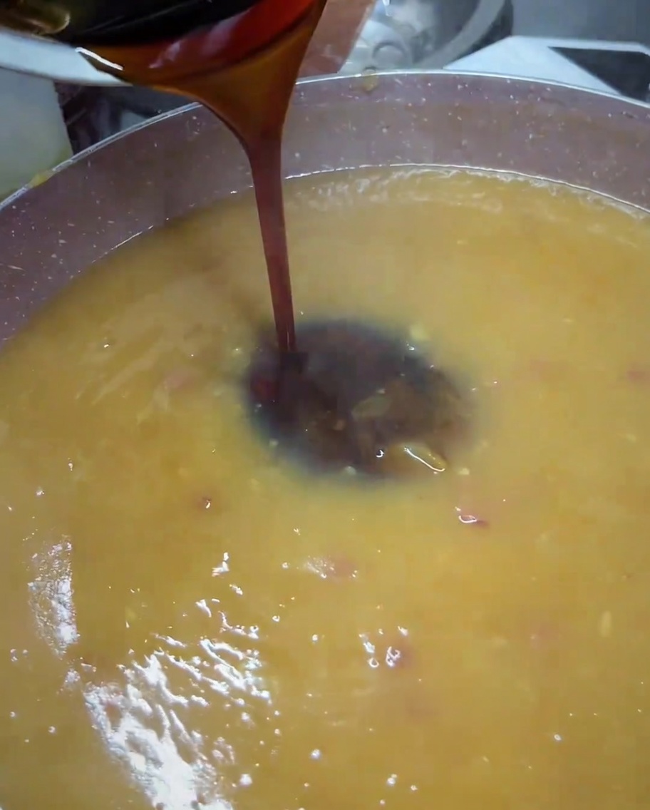 Dunkle Teriyaki-Sauce wird aus einer kleinen Schüssel in eine Pfanne mit gemixter, goldbrauner Sauce gegossen.