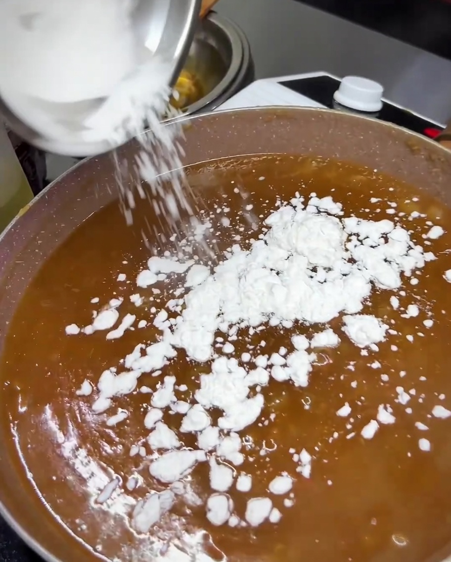 Tapiokastärke wird in die köchelnde Teriyaki-Sauce in der Pfanne gestreut.