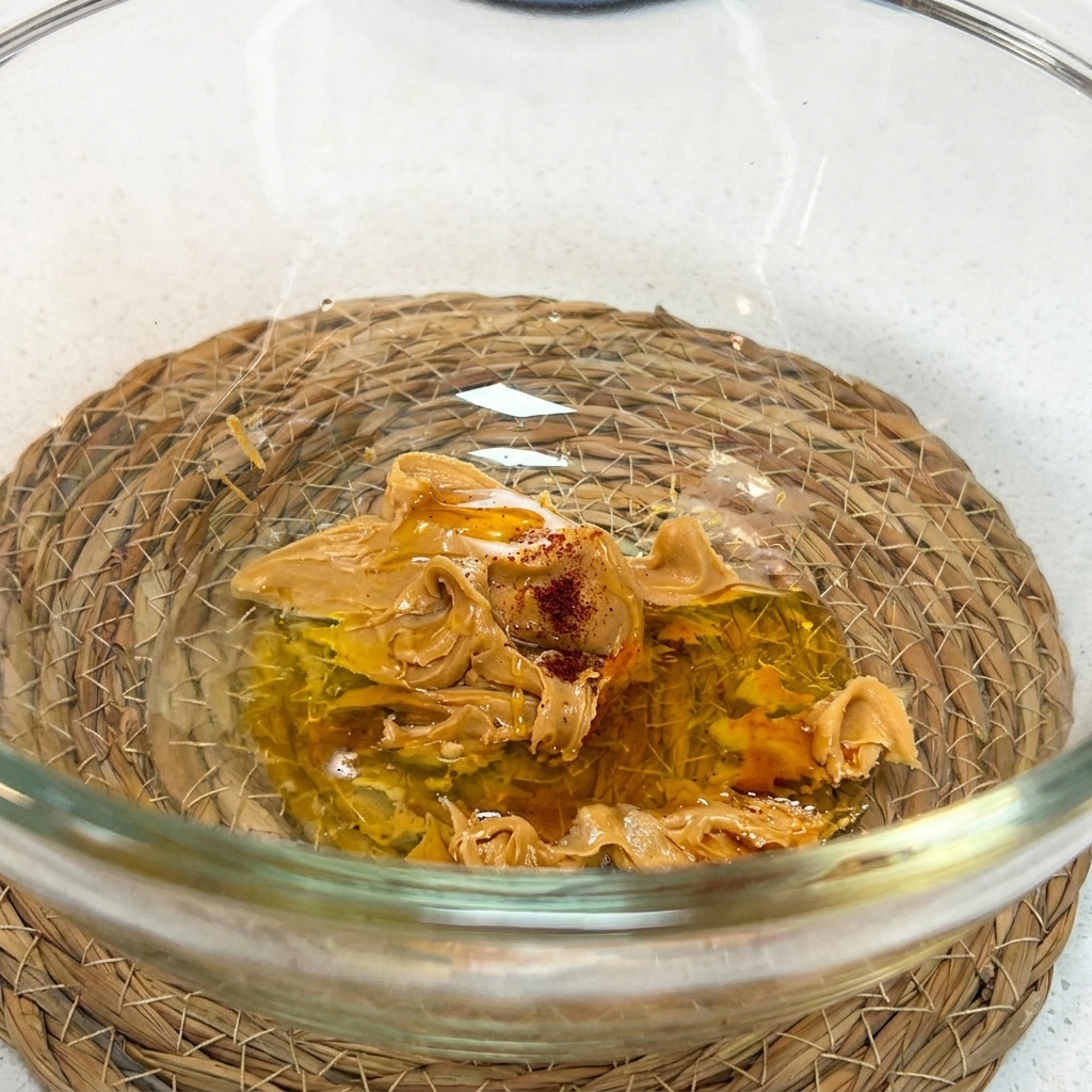Ein Schneebesen rührt Erdnussbutter, Sojasauce, Honig, Essig, Wasser und Shacha-Sauce in einer Schüssel zusammen.