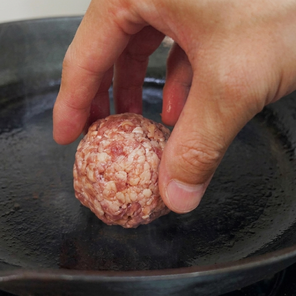 Rohe Rindfleischbällchen liegen bereit in einer vorgeheizten, flachen Pfanne.