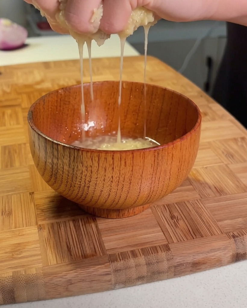 Hände beim Auswringen von geraspelten Kartoffeln über einer kleinen Holzschüssel.