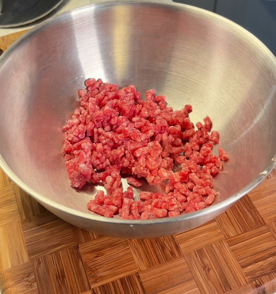 Rinderhackfleisch in einer Metallschüssel, bereit zum Würzen mit Schalotten, Salz und Pfeffer.
