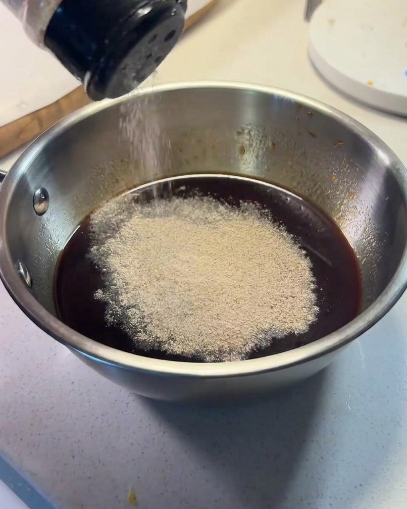 Soßenzutaten werden in einer kleinen Metallschüssel vermischt, schwarzer Pfeffer wird darüber gestreut.