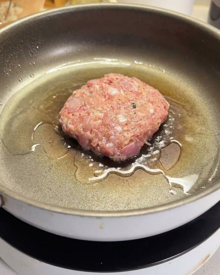 Ein rohes Rinderhack-Patty brutzelt in einer heißen, geölten beschichteten Pfanne.