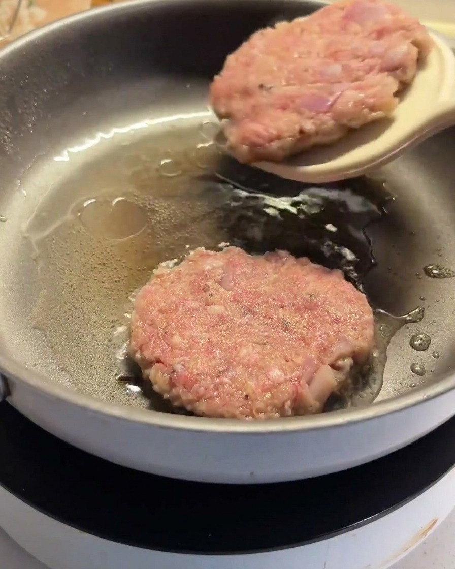 Ein Pfannenwender wendet ein bereits teilweise gebratenes Patty in der Pfanne.