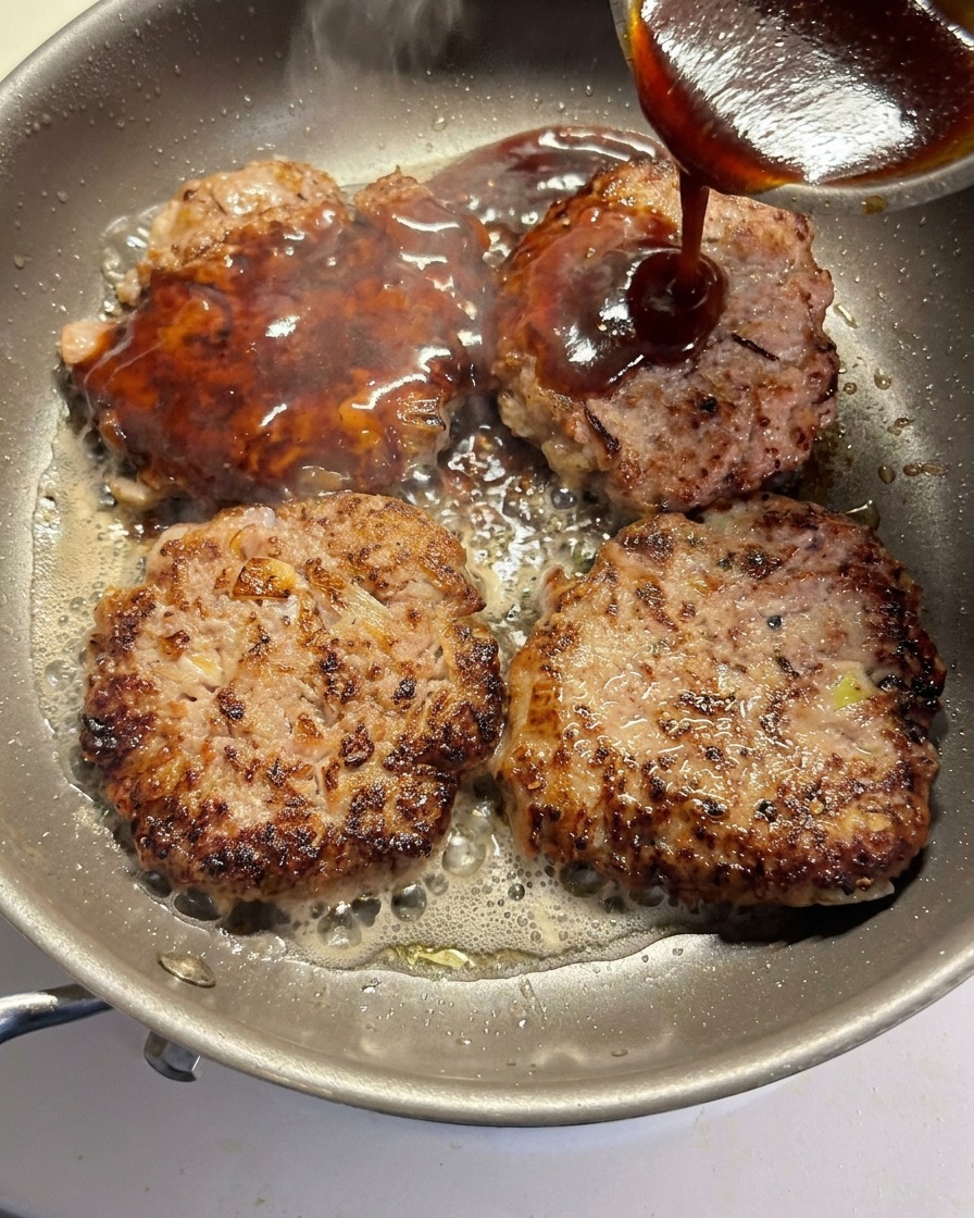 Die Soße wird über vier bräunende Rinder-Patties in der Pfanne gegossen.