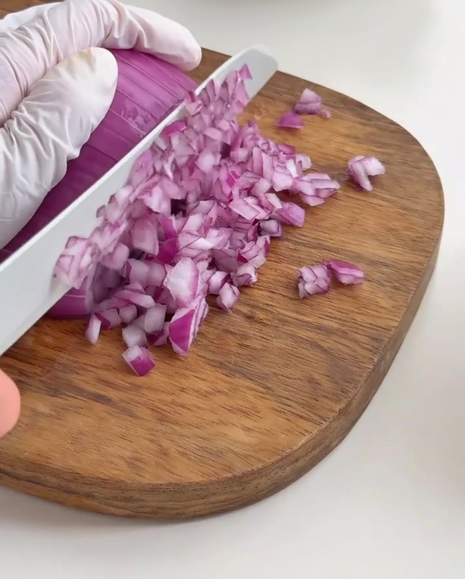 Fein gewürfelte rote Zwiebelstücke, ordentlich auf einem Holzbrett angerichtet.