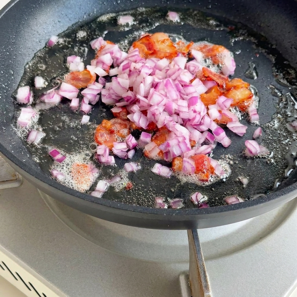 Gewürfelte Zwiebeln, Sellerie und Kartoffeln braten in einer Pfanne mit Speckresten.