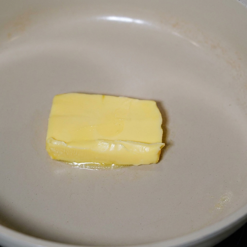 Speck brät in geschmolzener Butter in einer Pfanne.