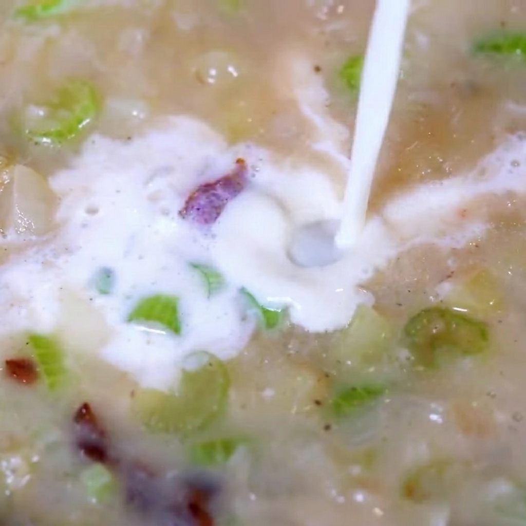Gehacktes Muschelfleisch wird in die köchelnde, cremige Suppe gegeben.
