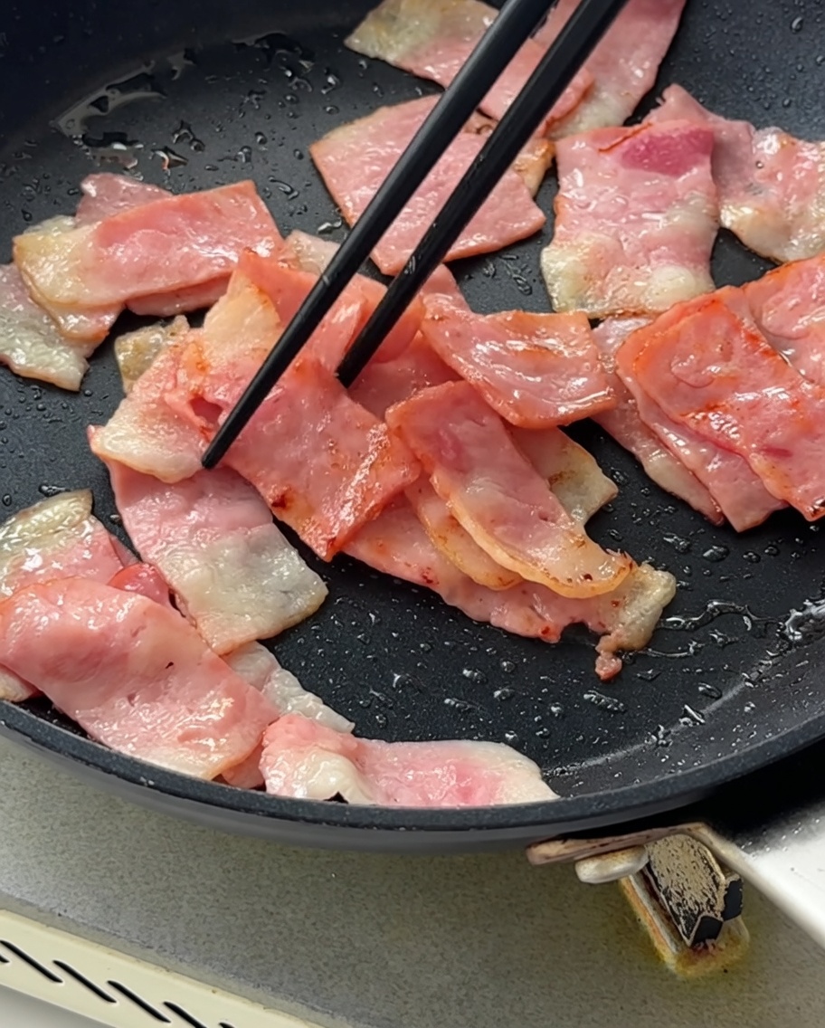Gewürfelte rote Zwiebeln werden in die Pfanne mit dem gebräunten Speck gerührt.
