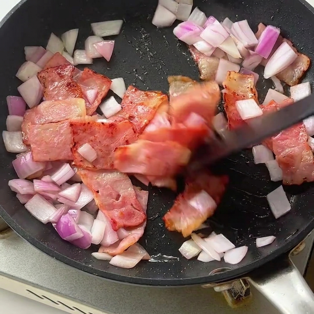 Fusilli-Nudeln und leuchtend grüner Spargel werden in die Pfanne mit Speck und Zwiebeln gegeben.