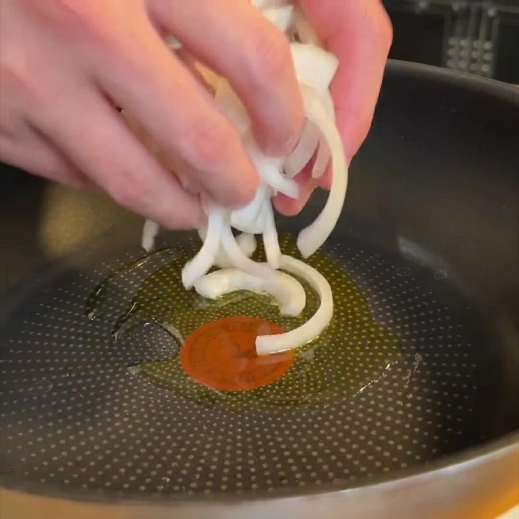 In dünne Scheiben geschnittene Zwiebeln, die in einer Pfanne mit Olivenöl glasig werden.