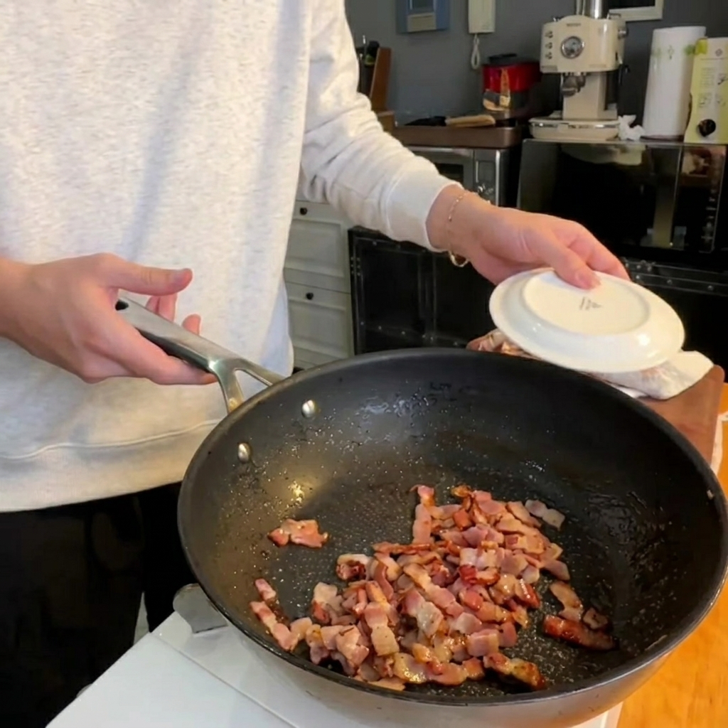 Frische Spargelspitzen braten in der Pfanne neben knusprigen Speckstücken.