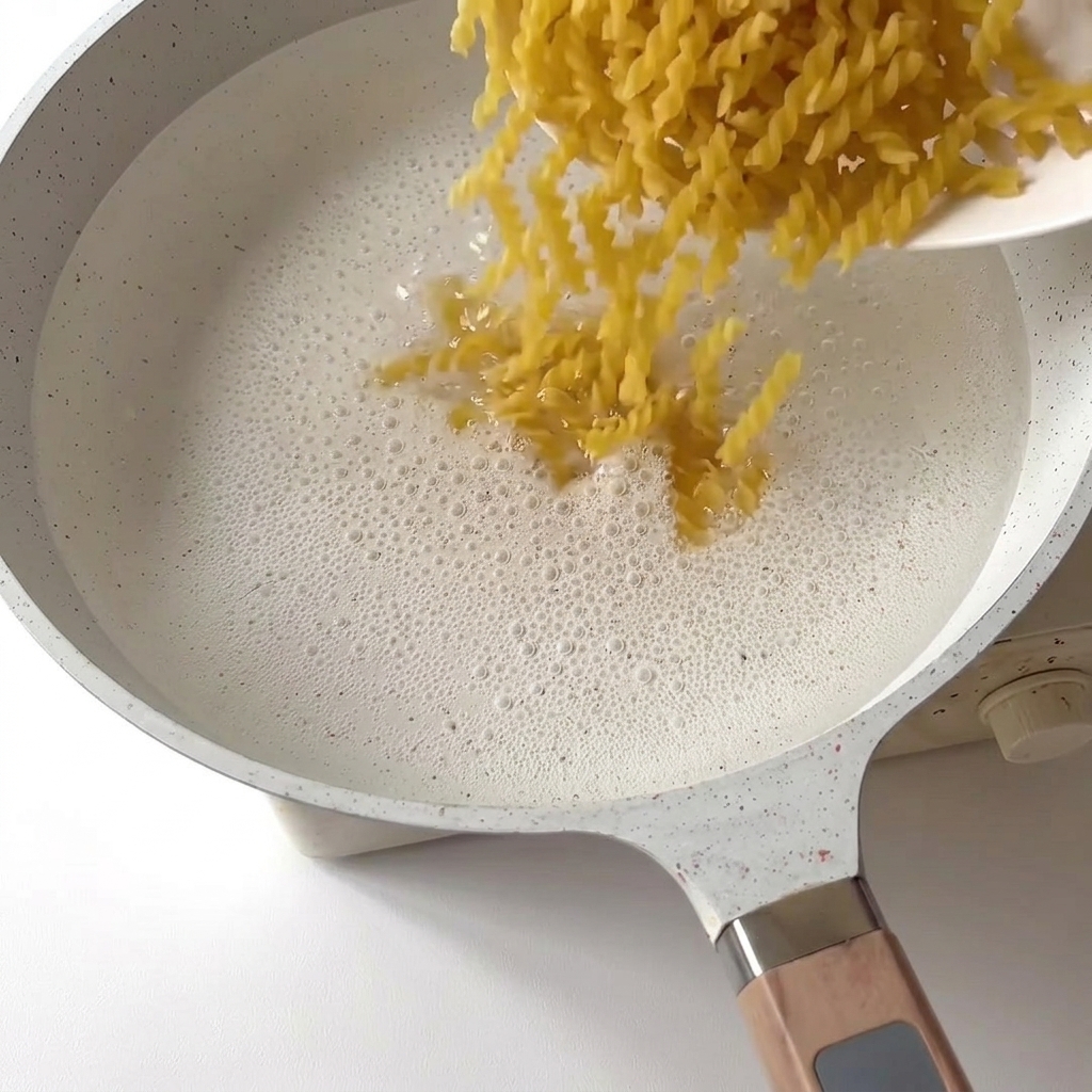Fusilli-Pasta fällt in einen Topf mit sprudelnd kochendem Wasser.