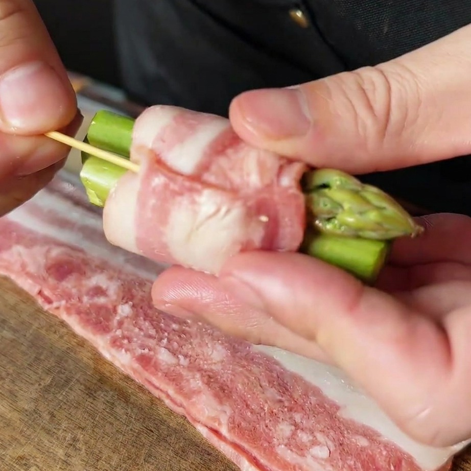 Ein mit Speck umwickeltes Spargelbündel, das mit einem Zahnstocher fixiert wird.