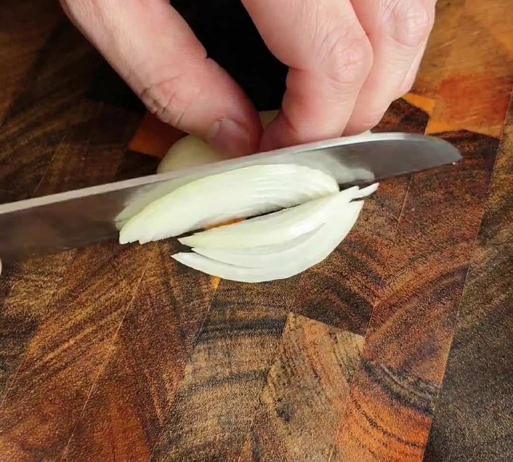 Ein Küchenmesser schneidet eine Zwiebel in feine Streifen auf einem Holzbrett.