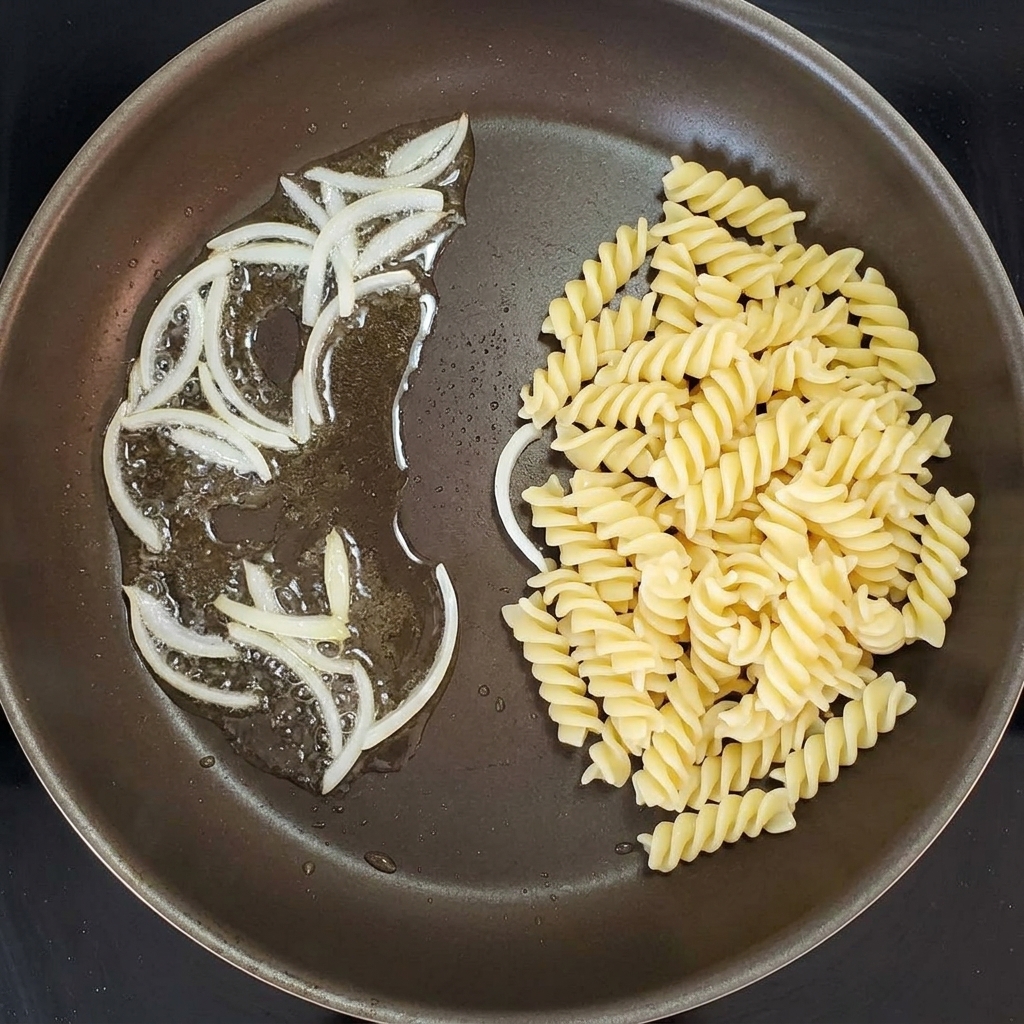 Spiralnudeln werden in einer Pfanne mit angeschwitzten Zwiebeln vermengt.