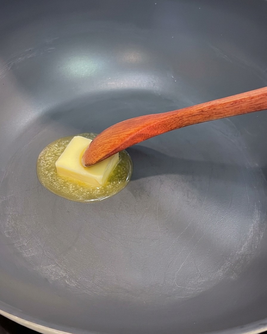 Butter schmilzt in einer Pfanne, rote Zwiebeln, Pilze und Spargel werden darin angebraten.