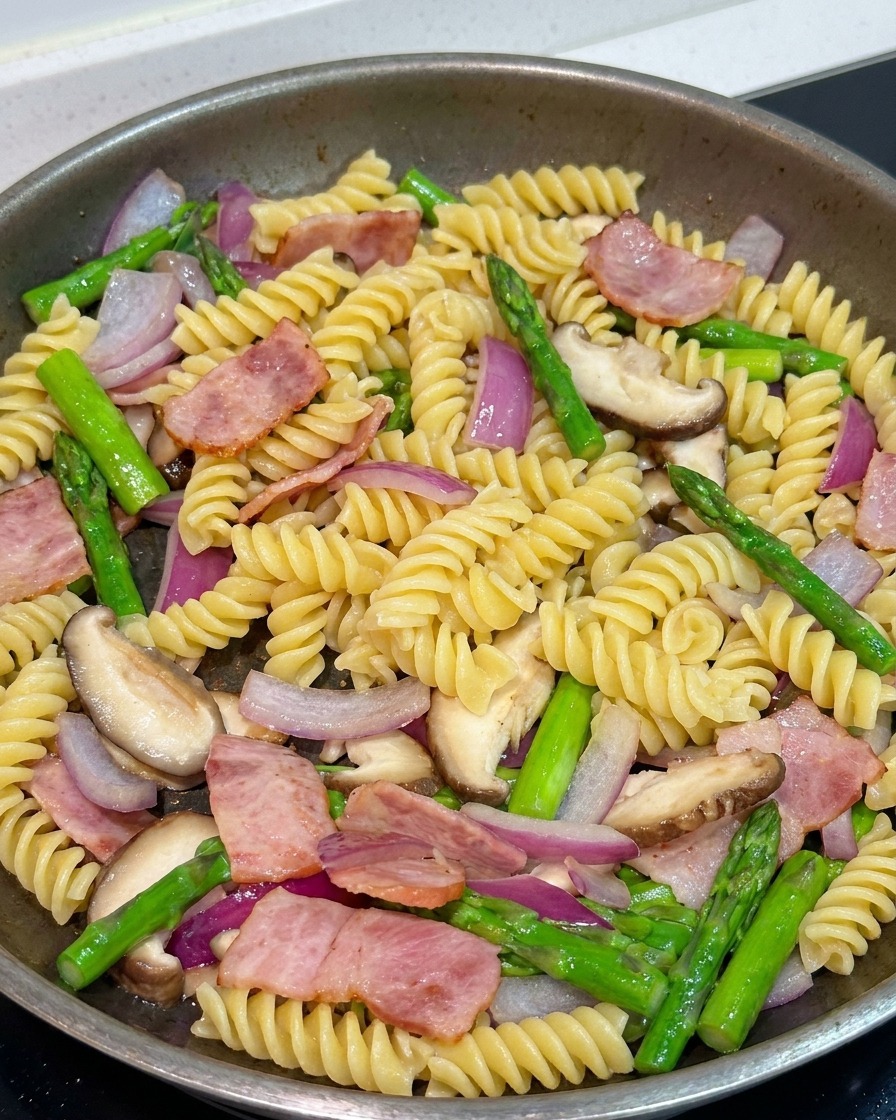 Pasta vermischt sich in der Pfanne mit Gemüse und Speck, wird mit Pfeffer und Sojasauce verfeinert.