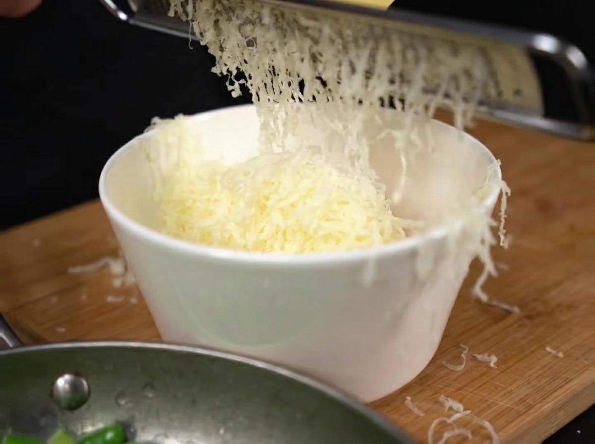Frisch geriebener Parmesan fällt auf die Eigelbe in einer Rührschüssel.