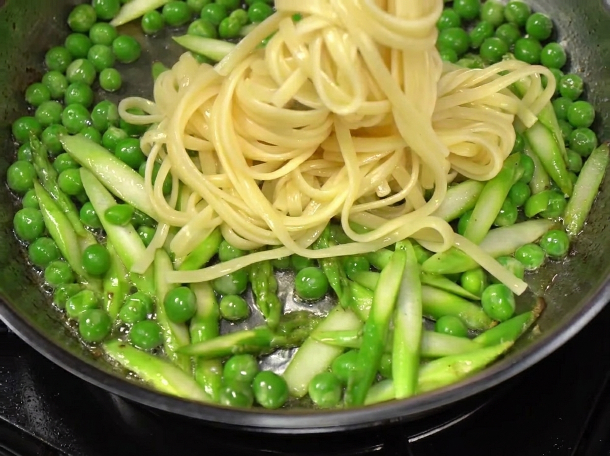 Spaghetti werden aus dem kochenden Wasser gehoben und in eine Pfanne mit gebratenem Gemüse und Speck gegeben.