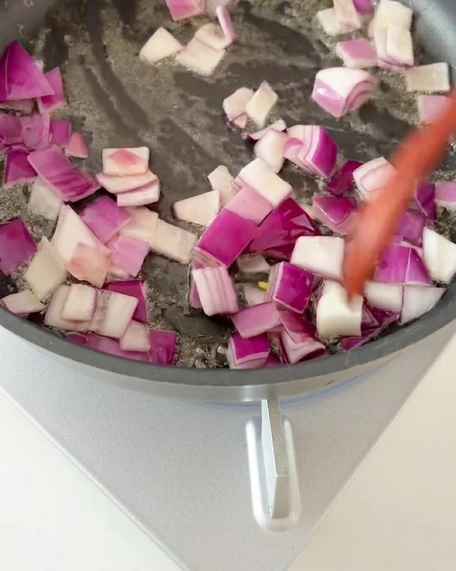 Rote Zwiebelwürfel werden in einer heißen Pfanne glasig gedünstet.