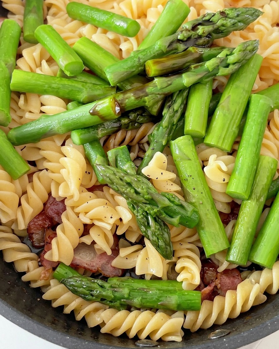 Eine Pfanne mit Fusilli, Spargel und Speck wird mit Saucen gewürzt.