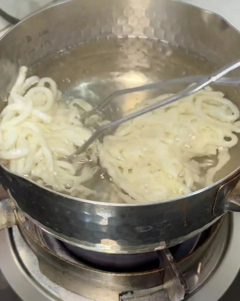 Udon-Nudeln werden mit einem Küchensieb aus einem Topf mit kochendem Wasser gehoben.