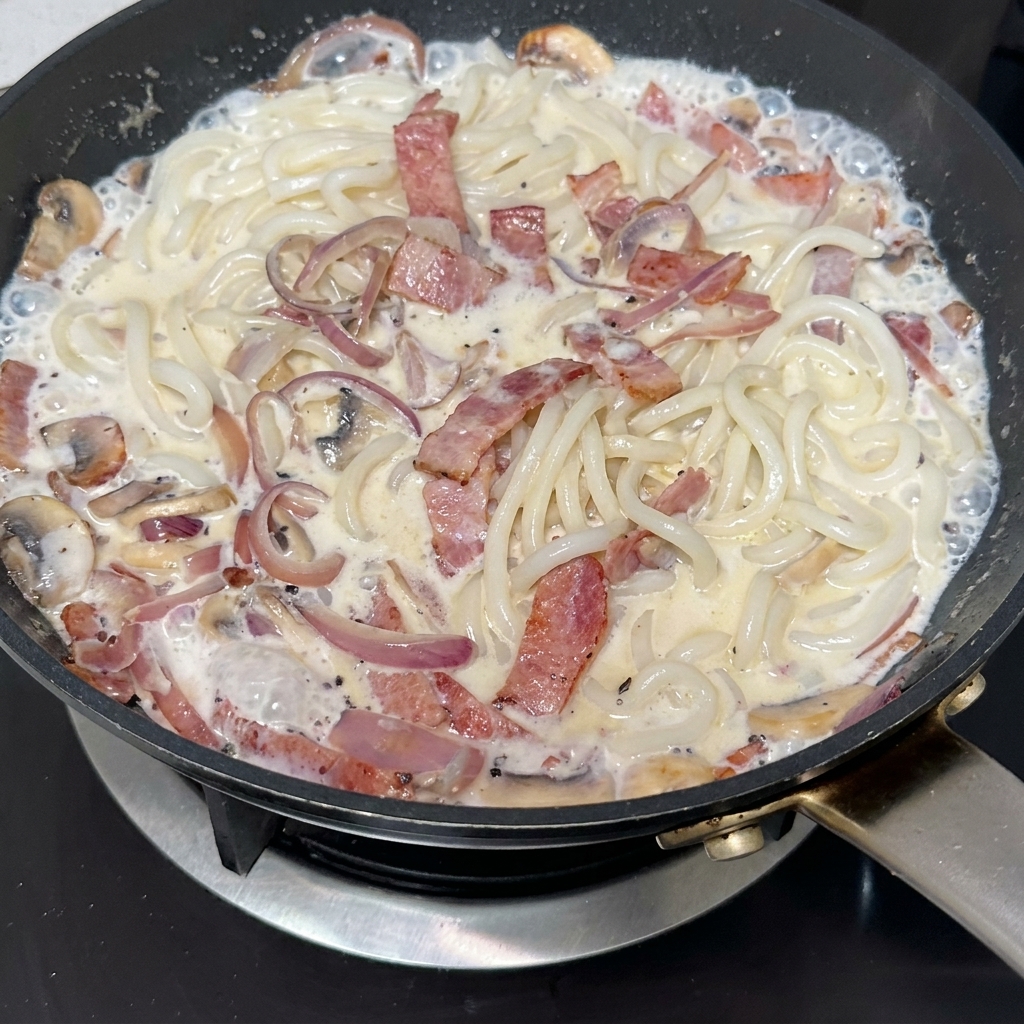 Schwarze Trüffelpaste wird in eine Pfanne mit knusprigem Speck, geschnittenen Pilzen und karamellisierten Zwiebeln eingerührt.