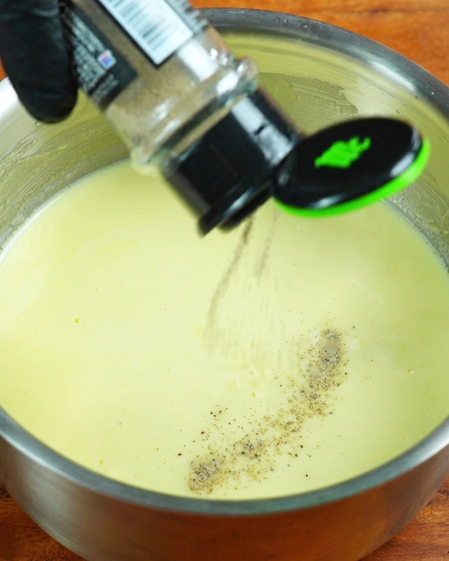 Sahne, weißer Pfeffer und Salz werden in die köchelnde Milchsoße gegeben.