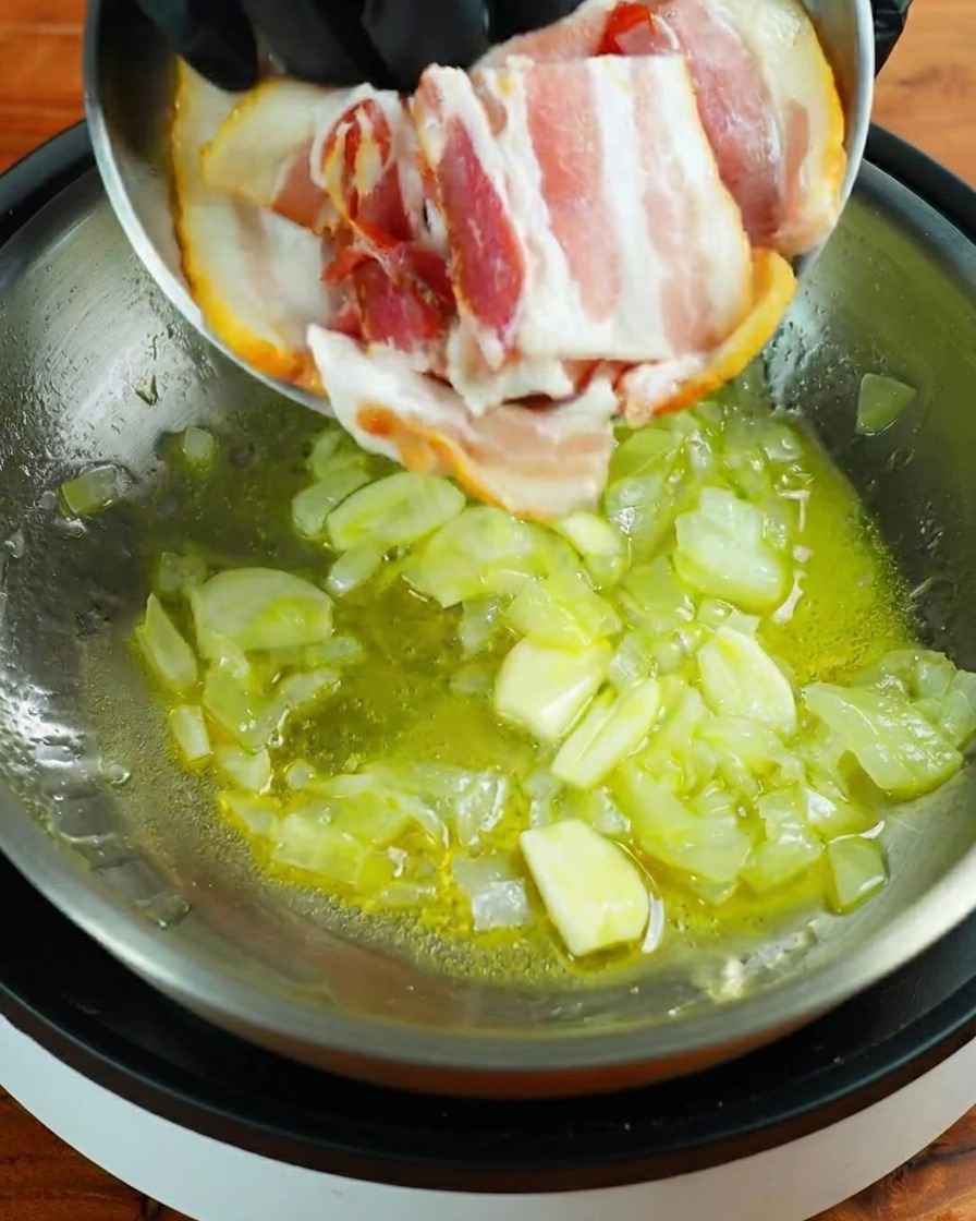 Drei Streifen roher Speck werden in die Pfanne zu Knoblauch und Zwiebeln gegeben.