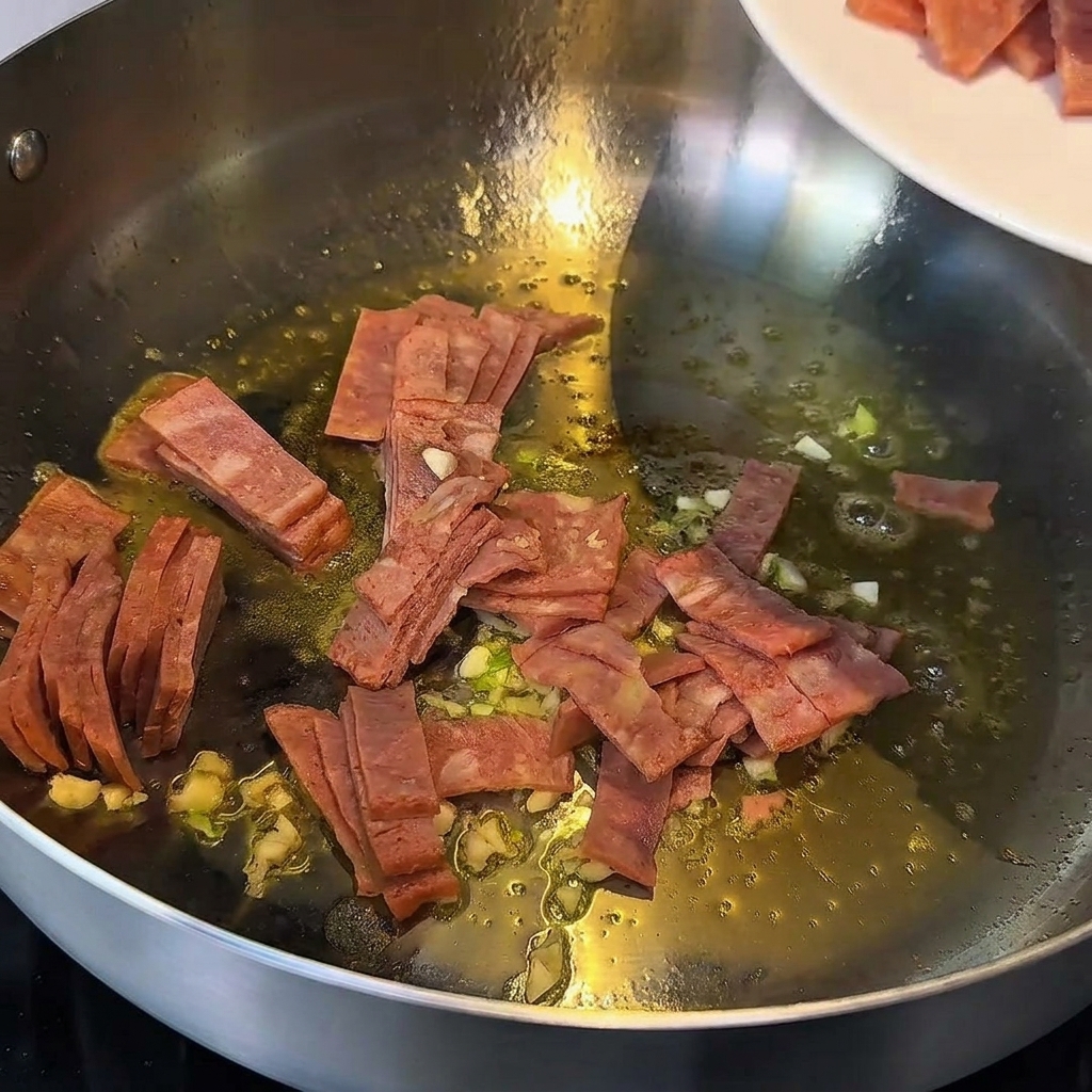 Knoblauch und Speckstücke, die in geschmolzener Butter in einer Metallpfanne angebraten werden.