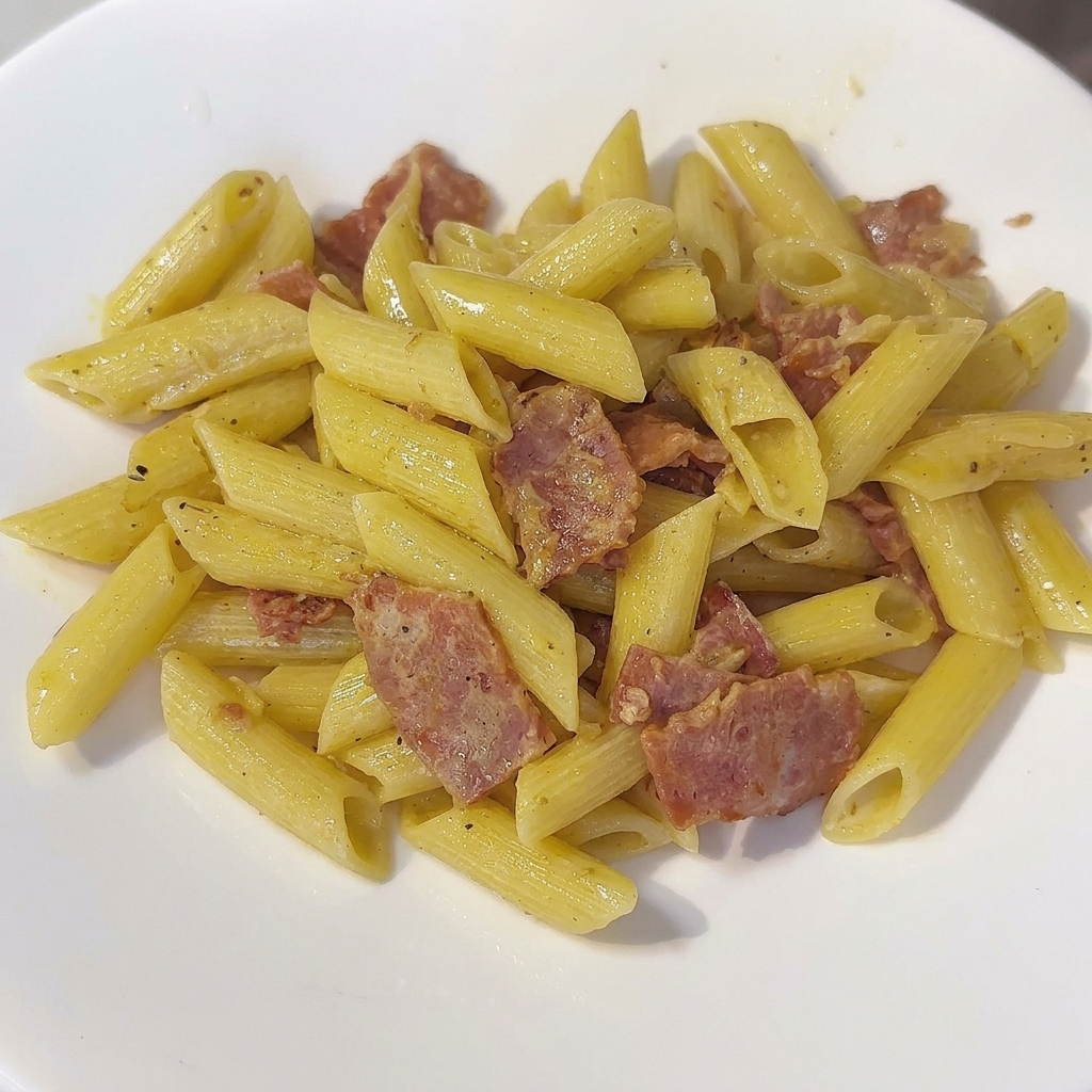 Eine Pfanne mit cremiger Penne-Pasta, die mit einem Pfannenwender umgerührt wird.