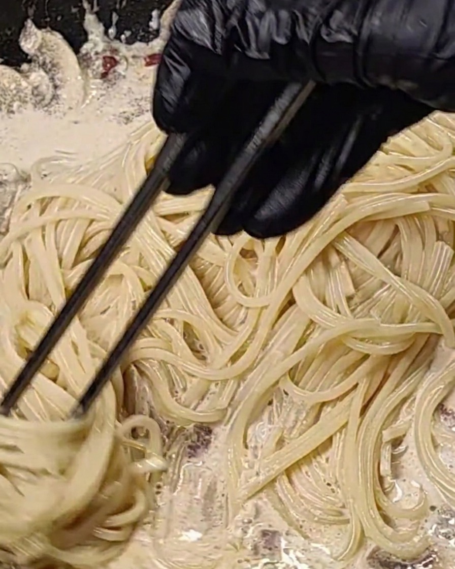 Die Spaghetti werden in der heißen Pfanne mit der Sauce vermengt.