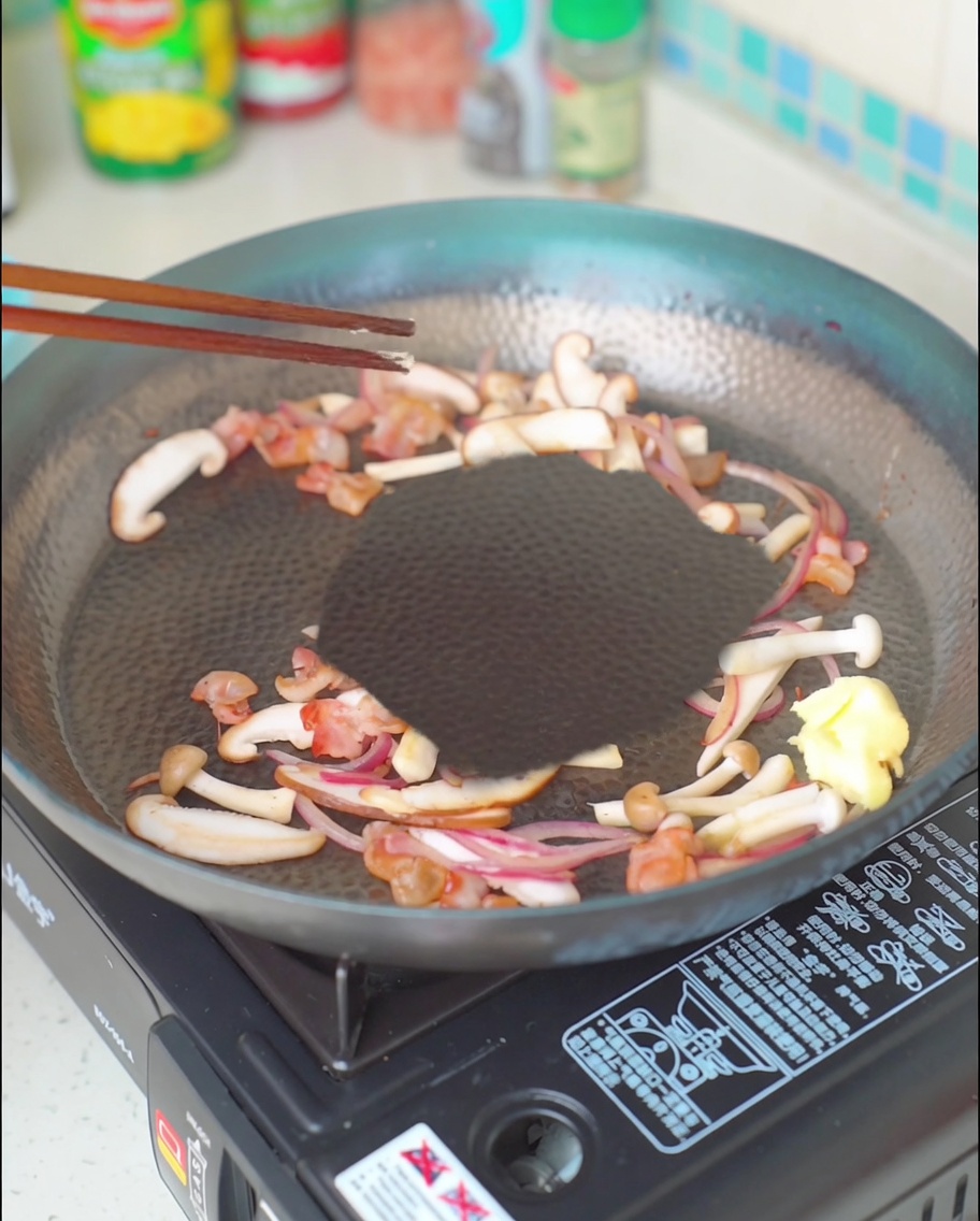 Ein Stück Butter schmilzt in der Speck-Pilz-Zwiebel-Mischung.