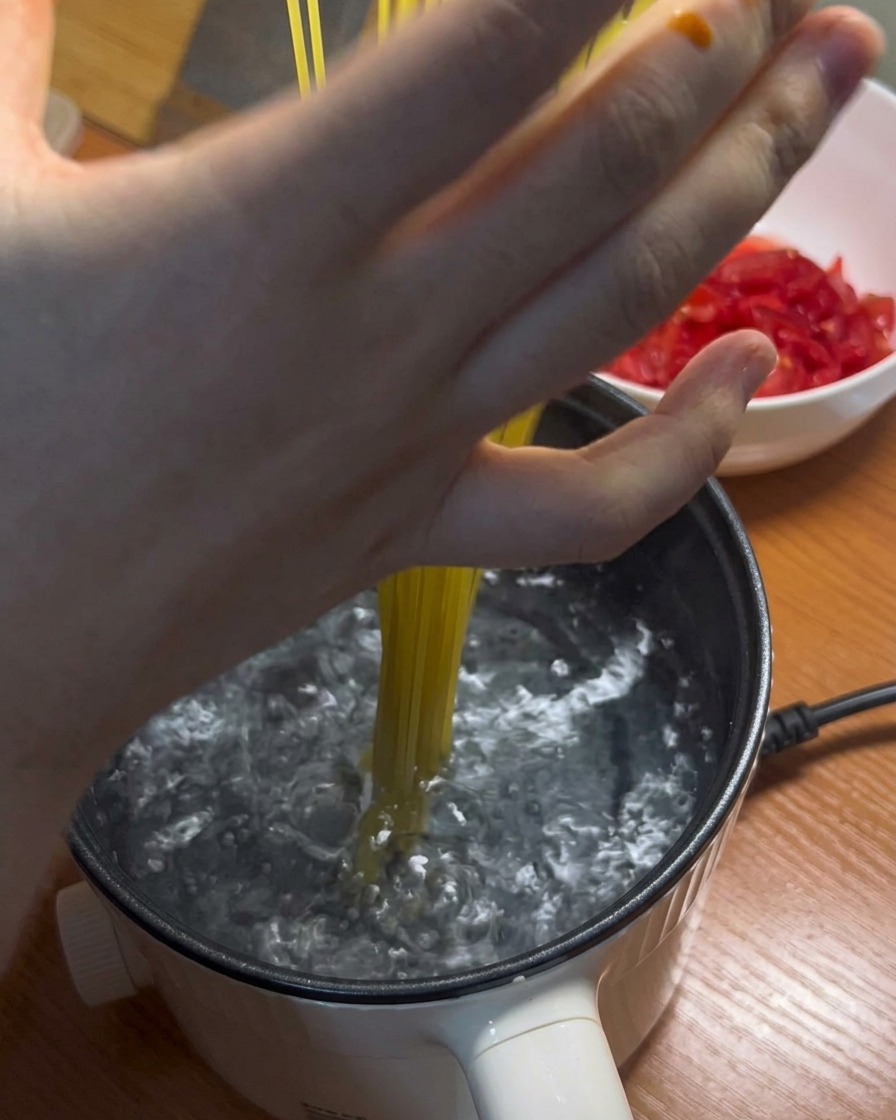 Lange Spaghetti-Nudeln werden in einen Topf mit kochendem Wasser gegeben.