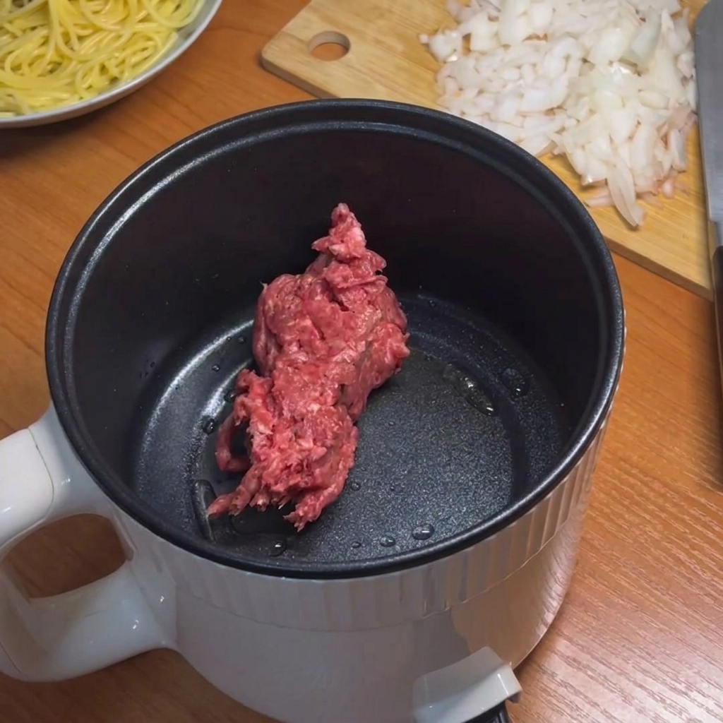 Hackfleisch wird in einem kleinen Topf mit einem Silikonspatel angebraten.