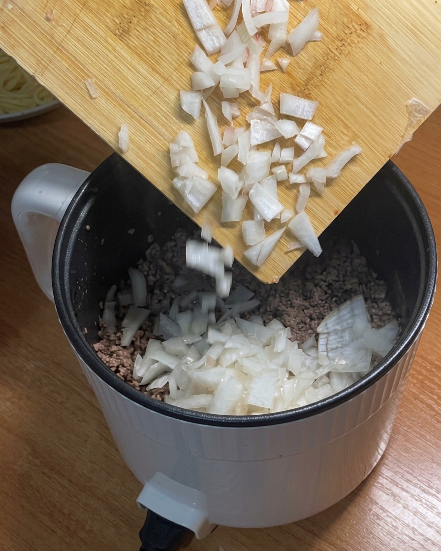 Gewürfelte Zwiebeln werden zum Hackfleisch in den Topf gegeben.