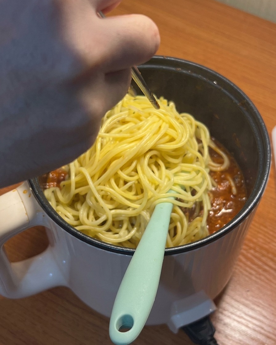 Gekochte Spaghetti werden in die köchelnde Sauce gegeben.