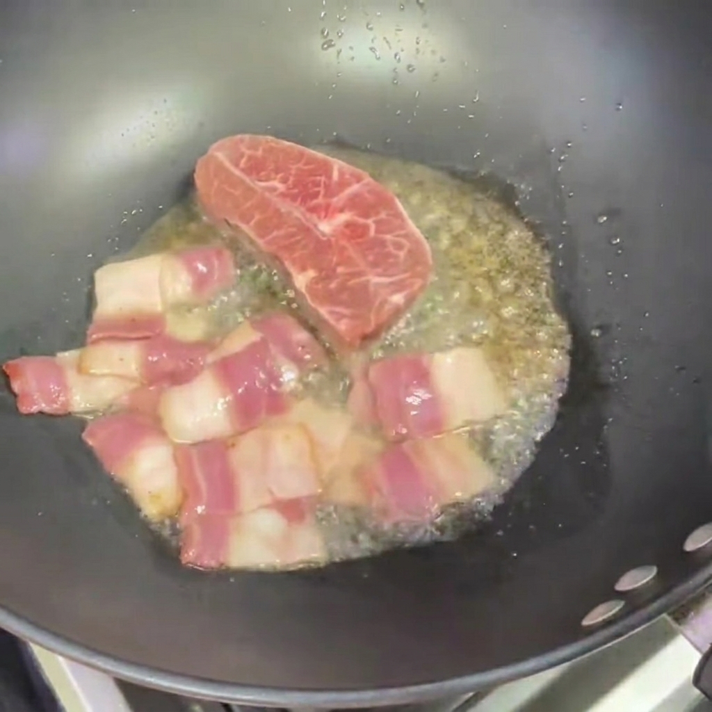 Zwei kleine Steaks braten im Wok neben Baconstücken.