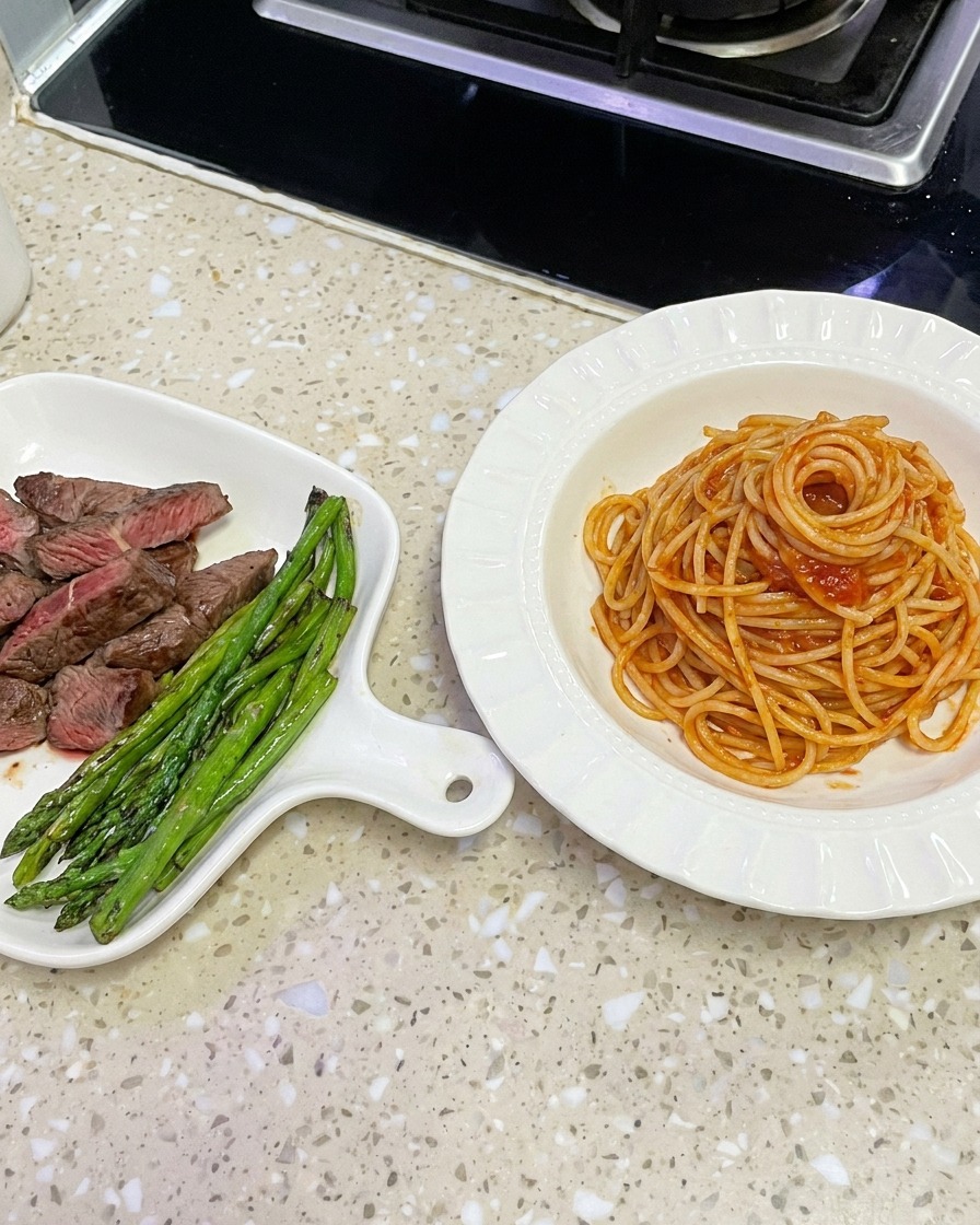 Saucenüberzogene Spaghetti werden mit einer Zange aus dem Wok gehoben, um sie in einer weißen Schüssel anzurichten.