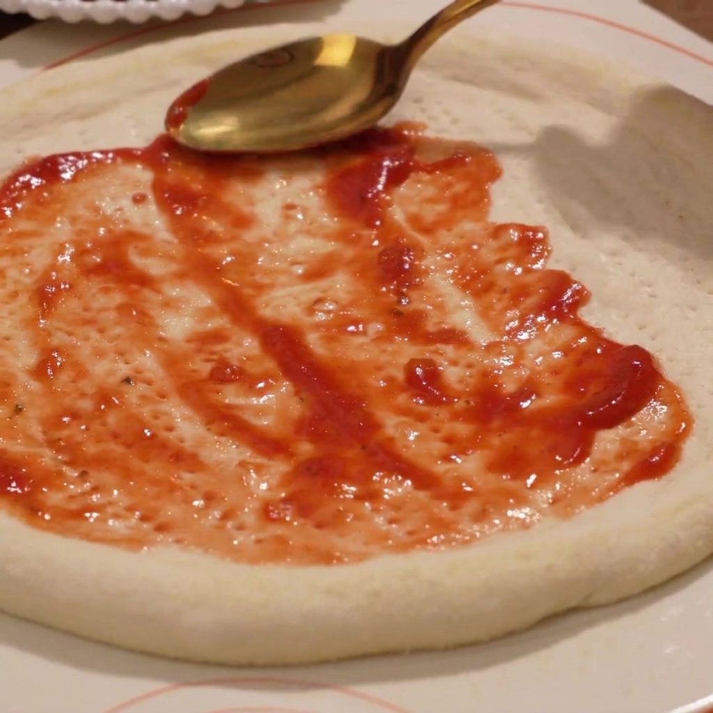Tomatensoße wird auf dem rohen Pizzateig verteilt.