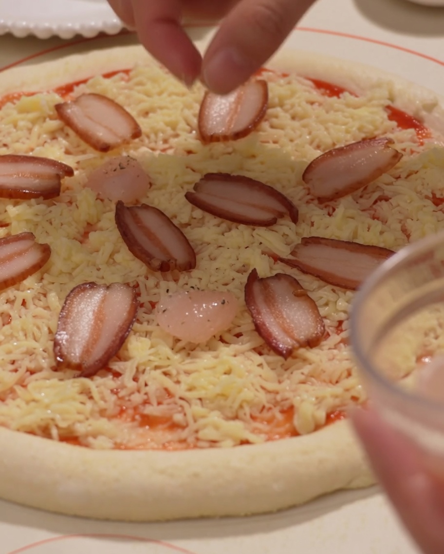 Schinken und Garnelen werden auf der Pizza platziert.